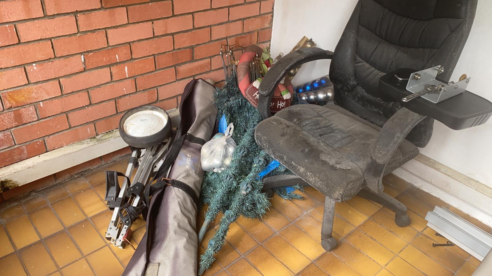 Artificial Christmas tree with decorations, worn office chair, and golf clubs stacked against a brick wall.