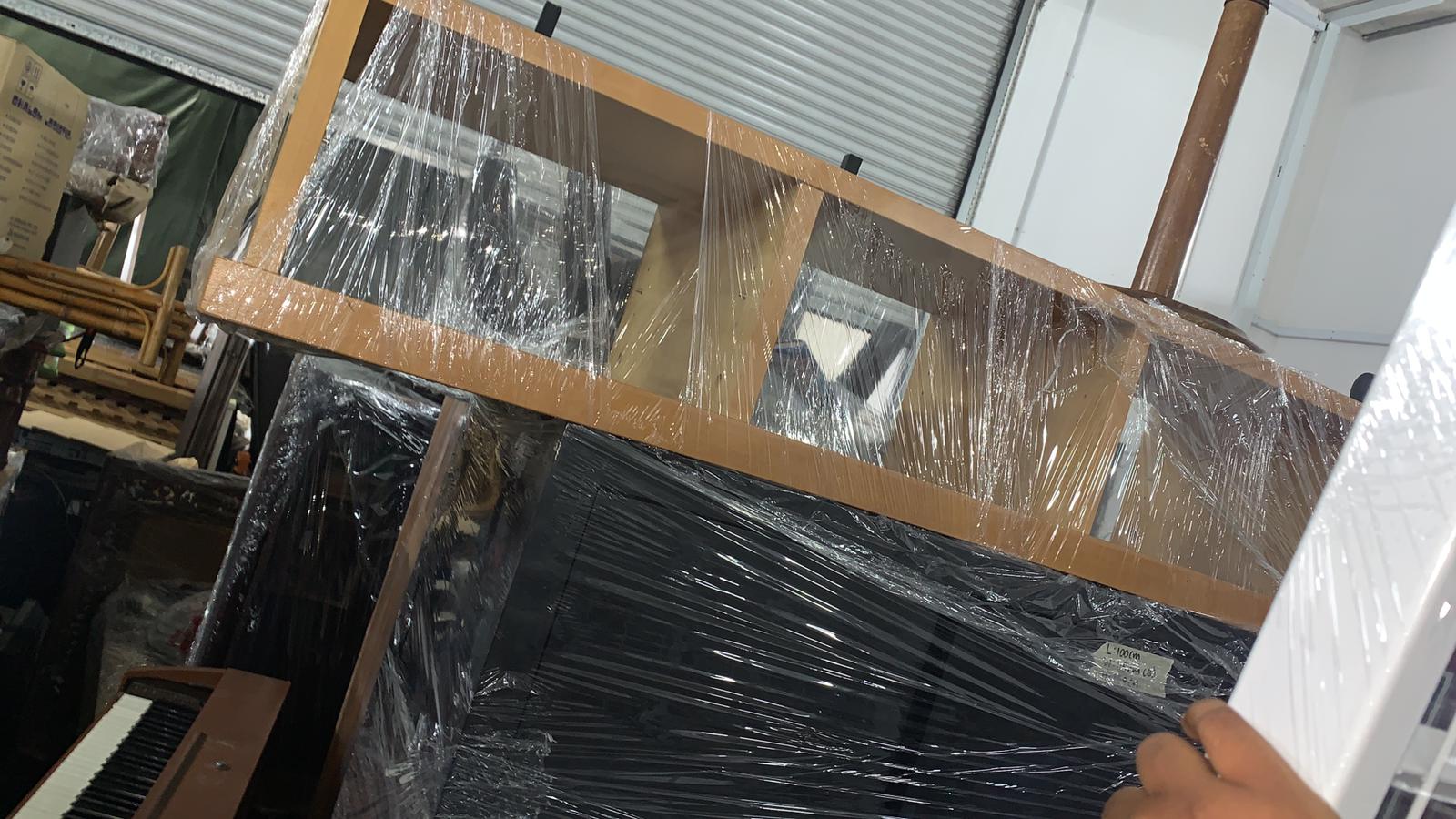 Wooden shelf unit and black furniture wrapped in plastic sheeting, ready for removal from a home.
