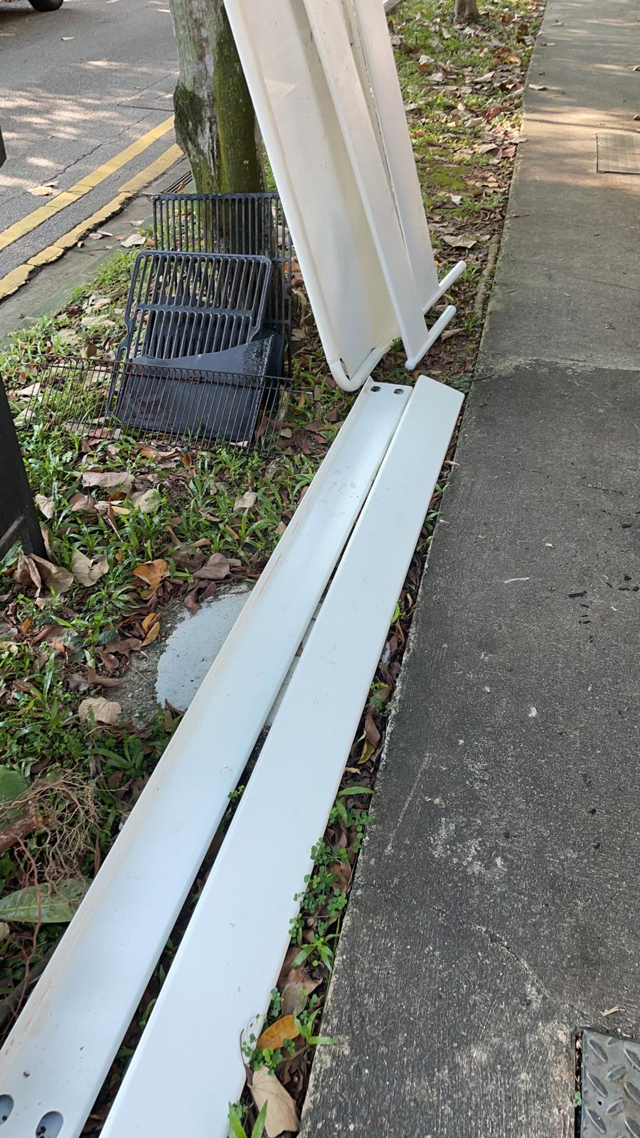 White panels and metal grates stacked by a tree and sidewalk, ready for removal.