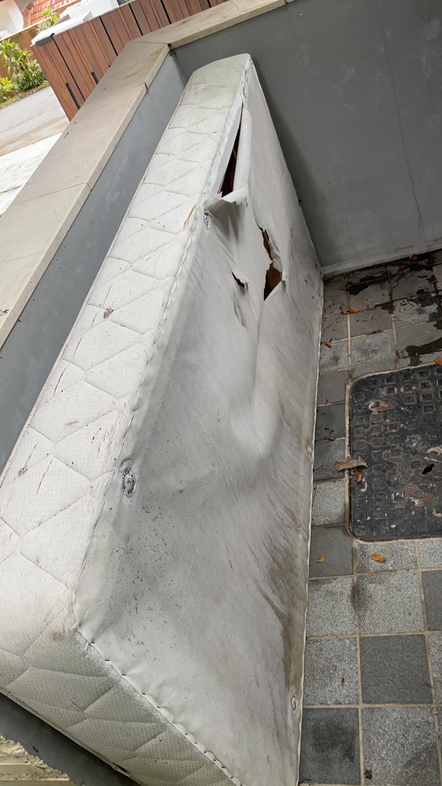 Torn white mattress with large rips lying on a tiled floor next to a metal drain grate.