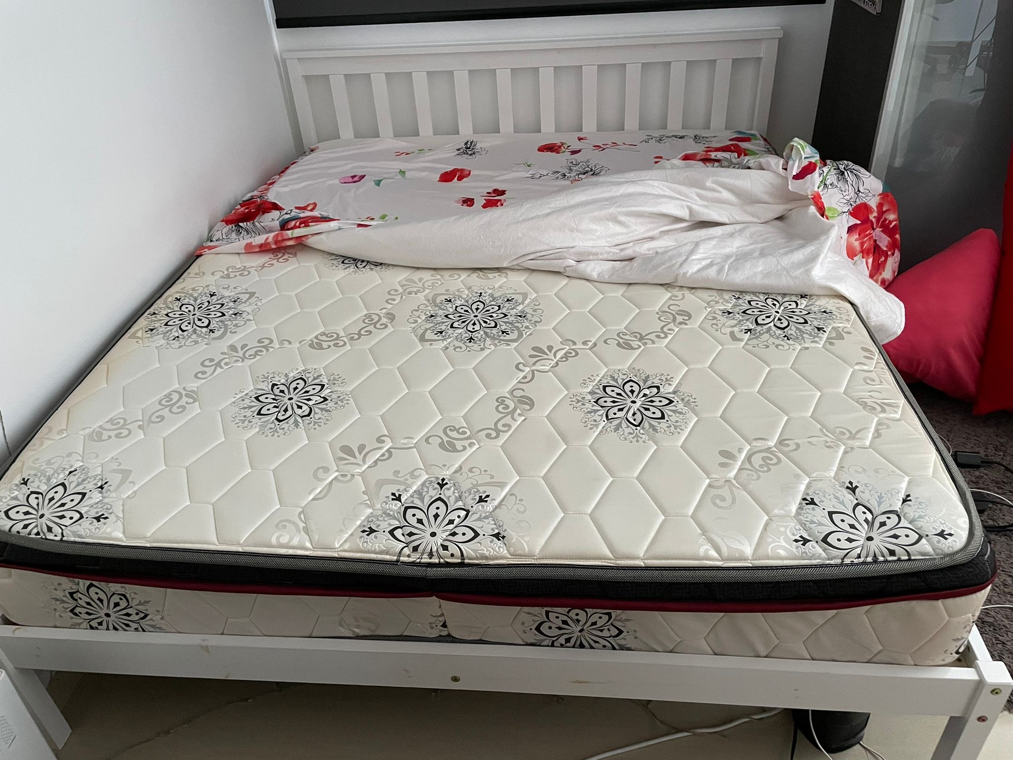 Older patterned double mattress on a white bed frame, ready for clearance — visible wear and faded print that puts it past charity-donation condition but still routine for paid pickup.