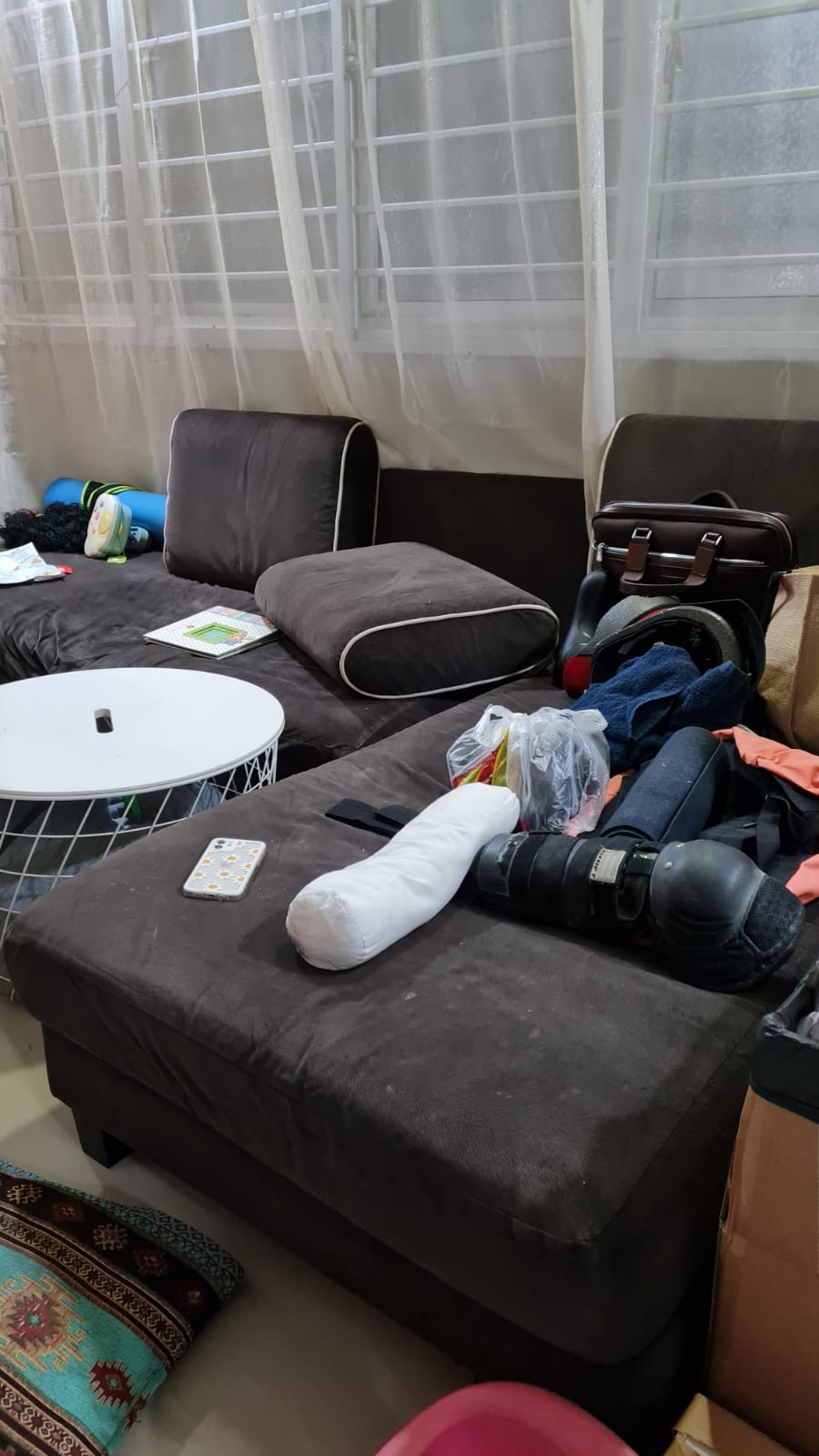 Dark brown sectional sofa piled with a white bolster pillow, phone, and protective gear among other clutter.
