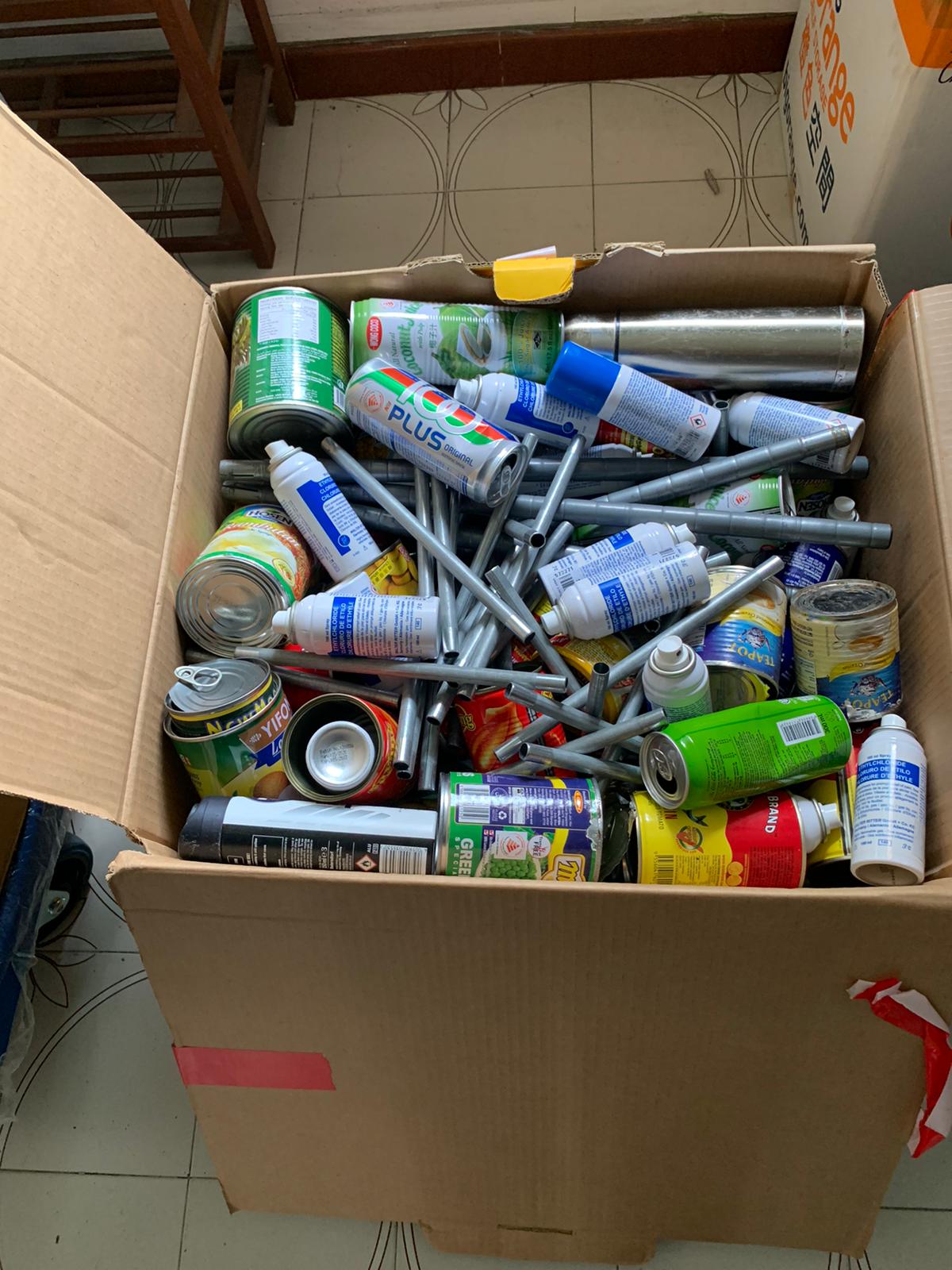 Cardboard box containing empty aluminum cans and spray cans ready for disposal.