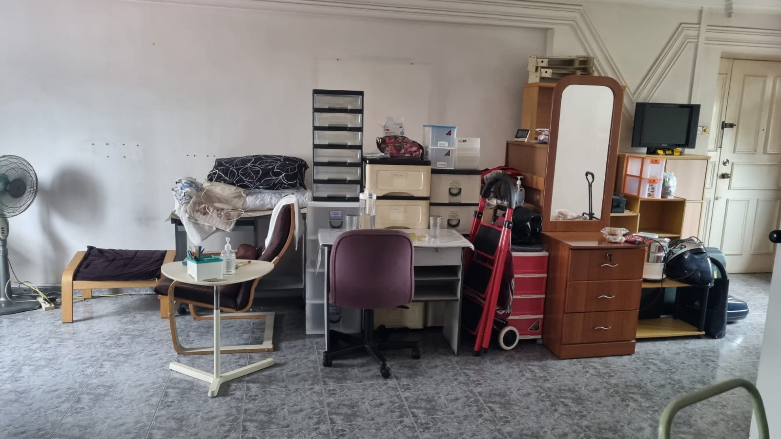 Residential room filled with wooden furniture, storage drawers, and scattered household items awaiting removal.