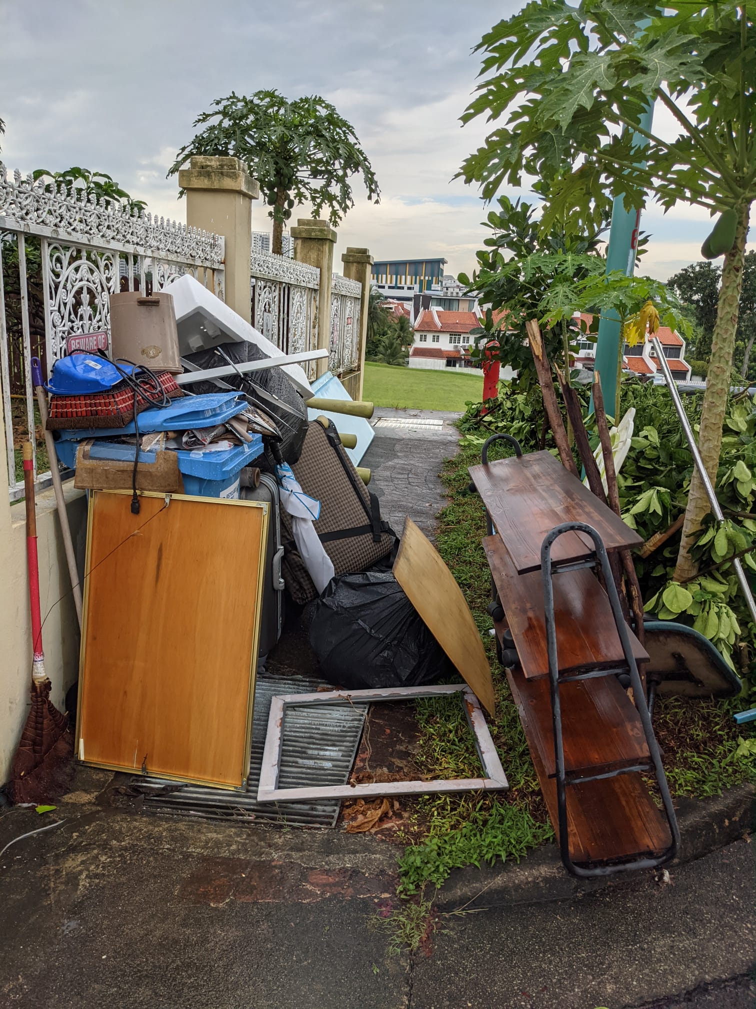 Pile of old furniture and household items stacked along a residential walkway beside a decorative fence.