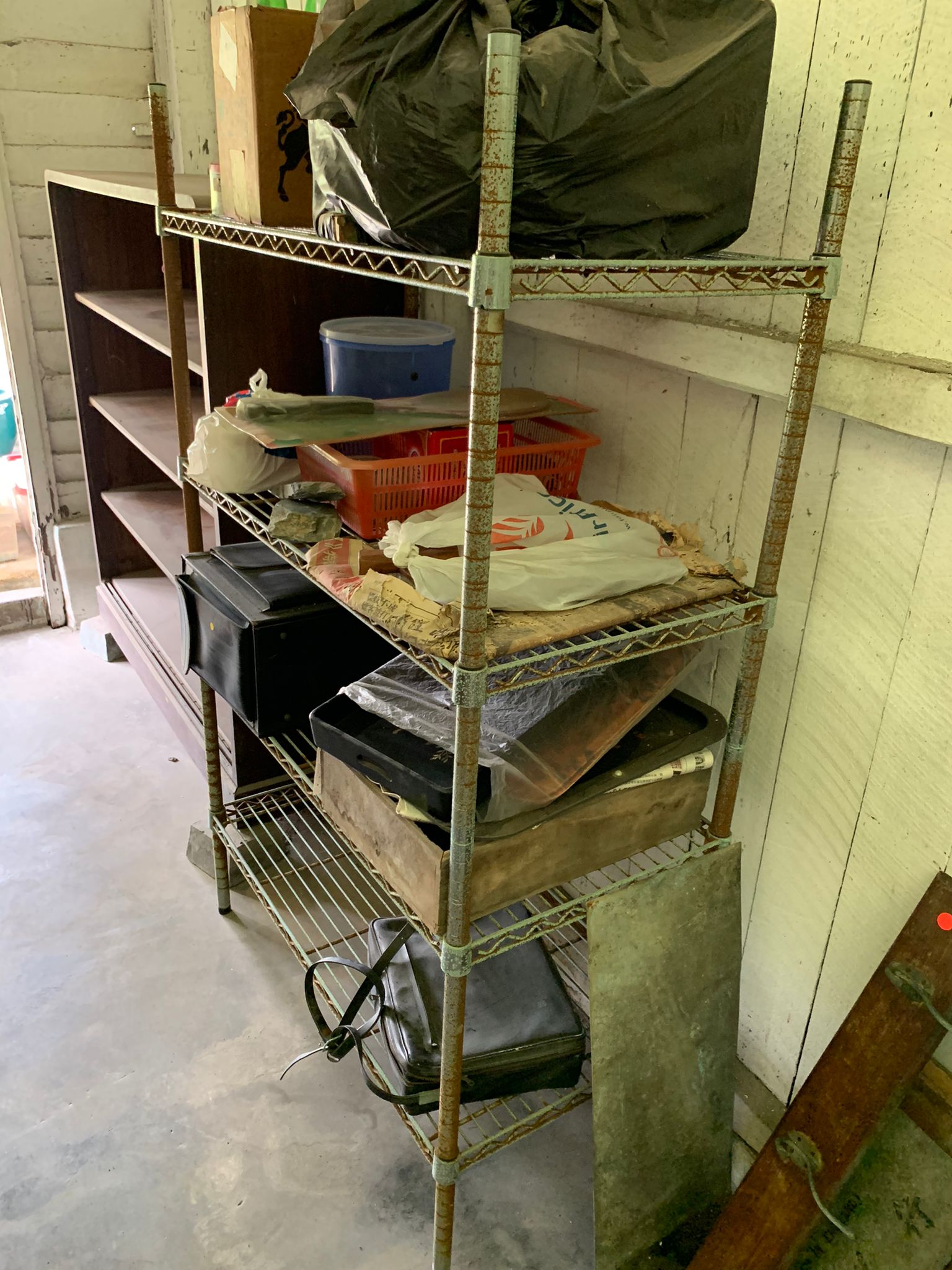 Metal shelving unit filled with household clutter, bags, and miscellaneous items stacked across multiple levels.