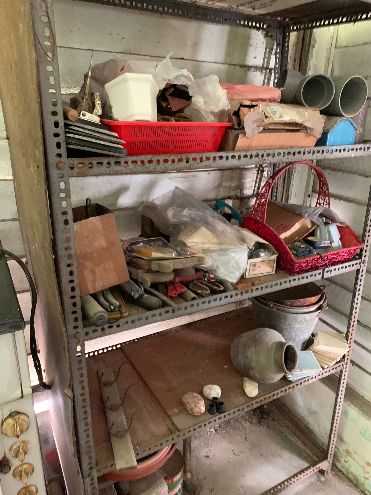 Shelving unit stacked with red storage basket, metal pipes, ceramic pots, and miscellaneous household items.