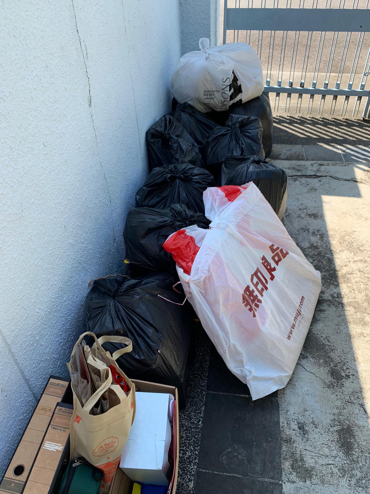 Pile of black and white trash bags stacked against a white wall, with a white shopping bag bearing red Chinese characters placed in front.