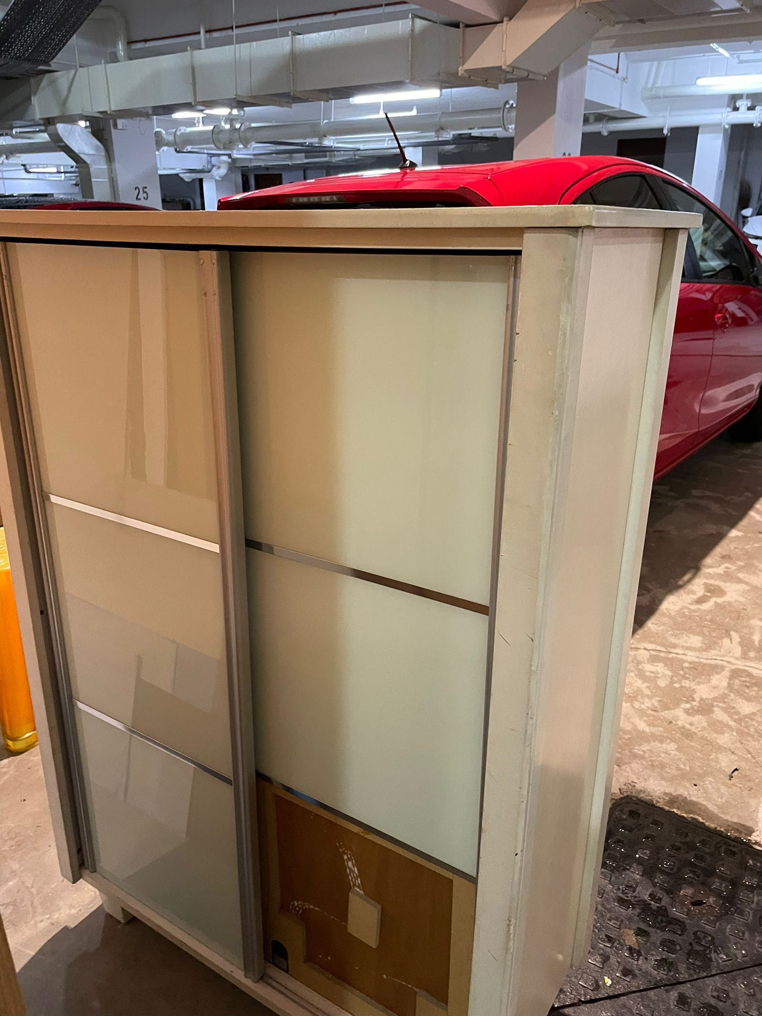 Light-coloured sliding door wardrobe standing in a parking lot, ready for disposal.