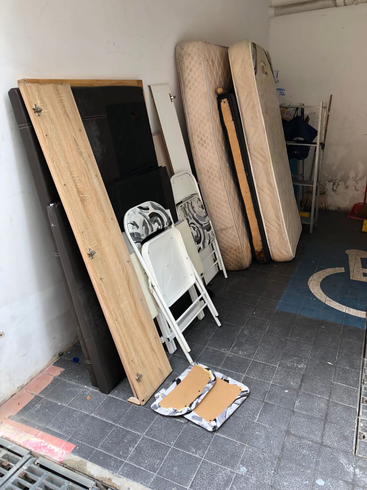 Stacked mattresses, bed frames, and folding chairs awaiting disposal at a residential location.