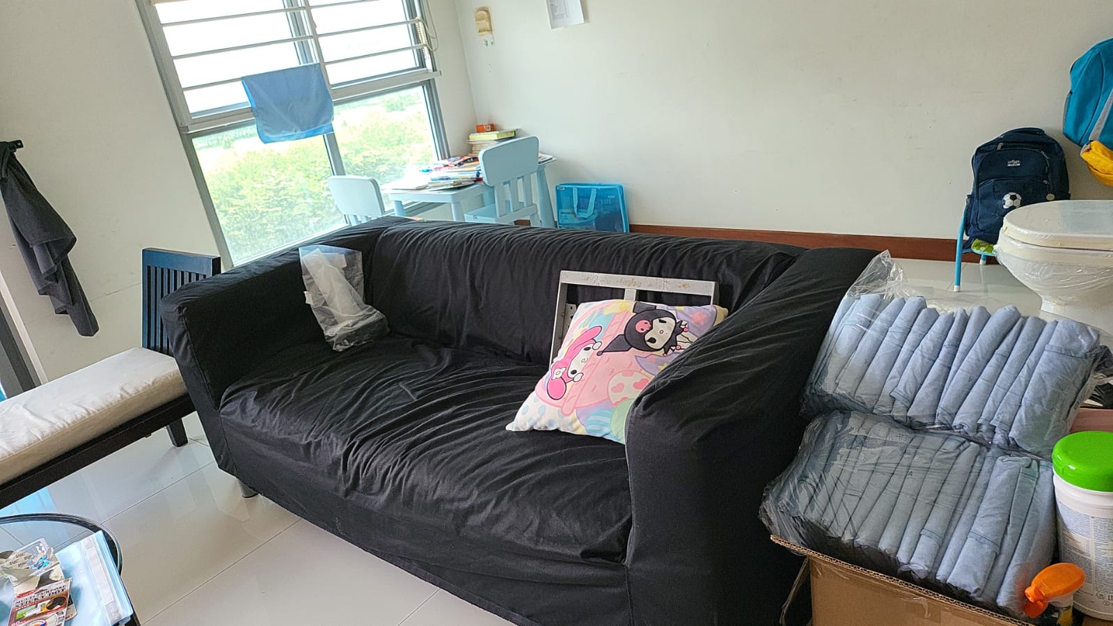 Black sofa with decorative pillow and stacked bags of folded clothing in a residential living room.