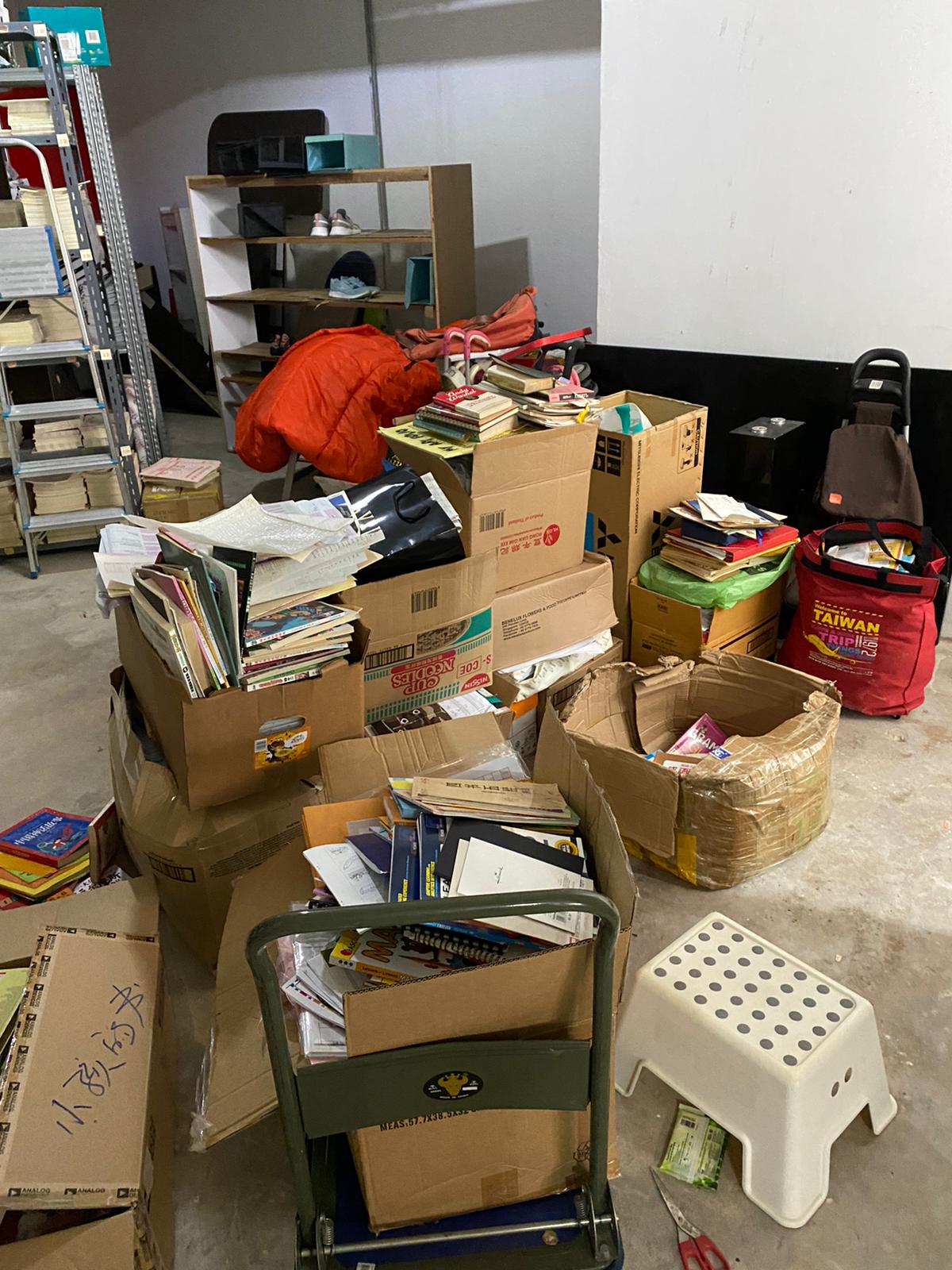 Cardboard boxes, stacked books, and household items arranged on a floor and hand trolley awaiting collection.